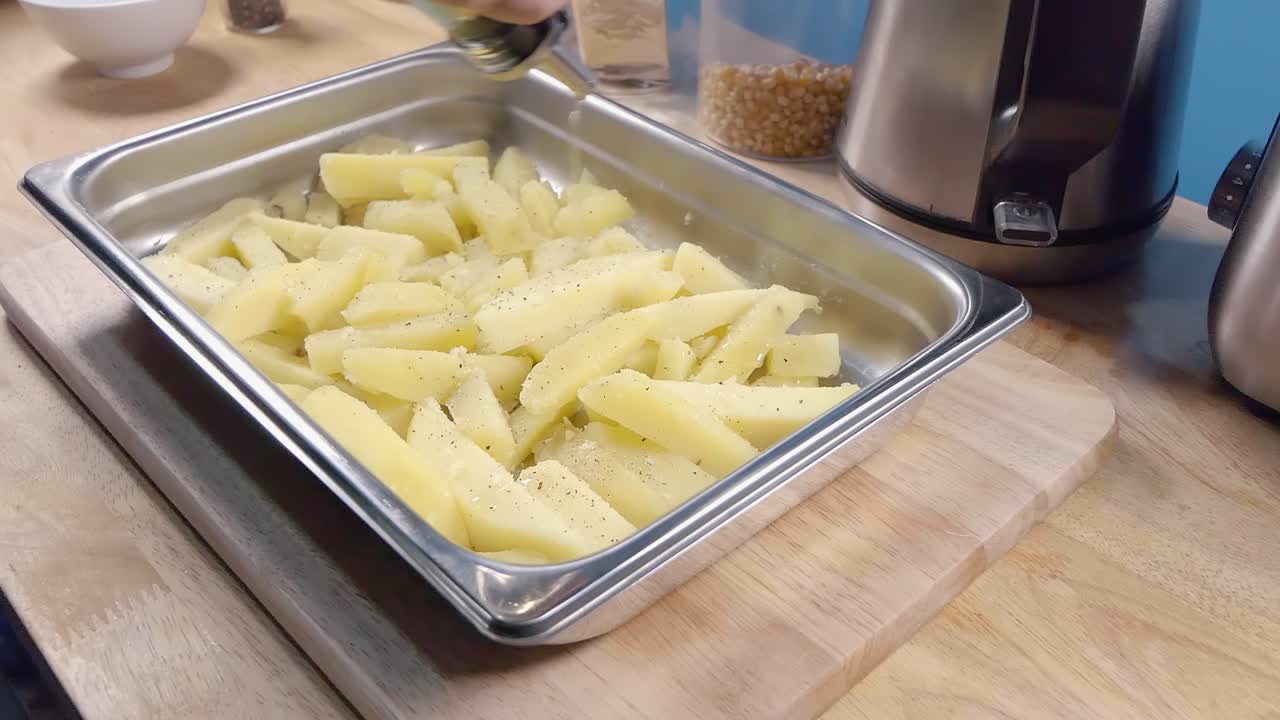 tiro deslizante en cámara lenta de aceite lloviznando en papas fritas caseras en una bandeja de metal para hornear antes de cocinar en la cocina