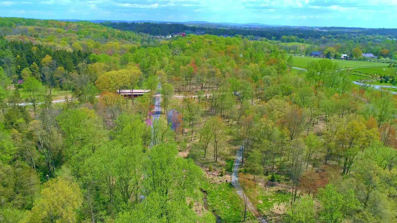 vista aérea de los colores primaverales de un bosque con un puente cubierto y una vía férrea en un día soleado