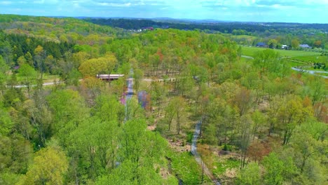 Vista-Aérea-De-Los-Colores-Primaverales-De-Un-Bosque-Con-Un-Puente-Cubierto-Y-Una-Vía-Férrea-En-Un-Día-Soleado