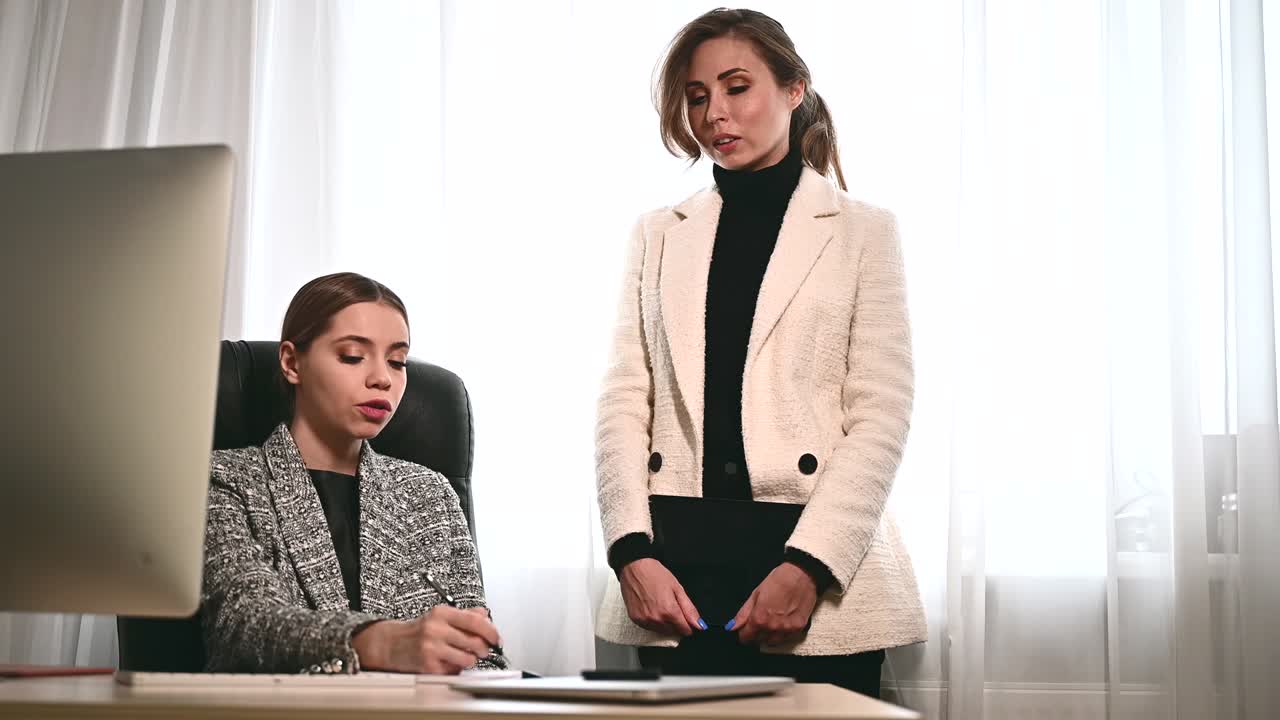 Attractive young adult women work together in the office at a meeting. A new employee consults with a mentor and presents a new project. Open space concept for teamwork