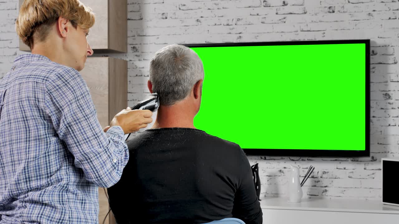 home haircut wife cuts husband hair while watching tv with green screen
