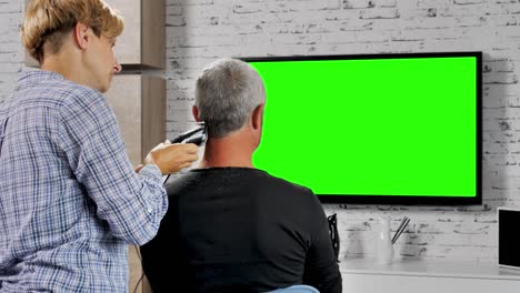 가정 헤어스타일 아내는 초록색 화면으로 tv를 보는 동안 남편의 머리카락을 잘라