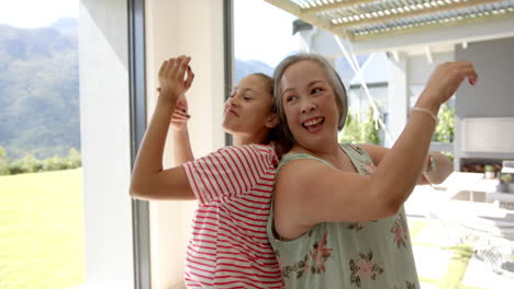 asian grandmother and biracial granddaughter are dancing joyfully indoors