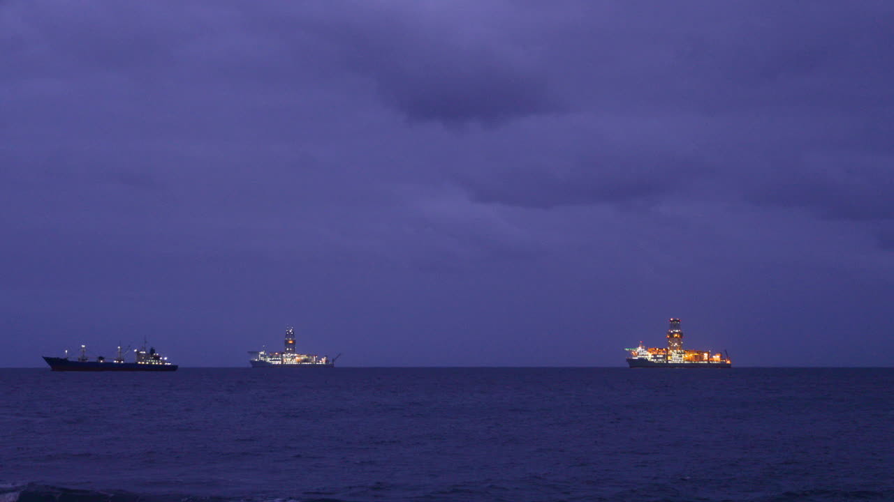 Several food processing boats moored in the distance at sea during the night illuminated by the lights glowing on the horizon during high tide 4k slow motion capture at 60fps