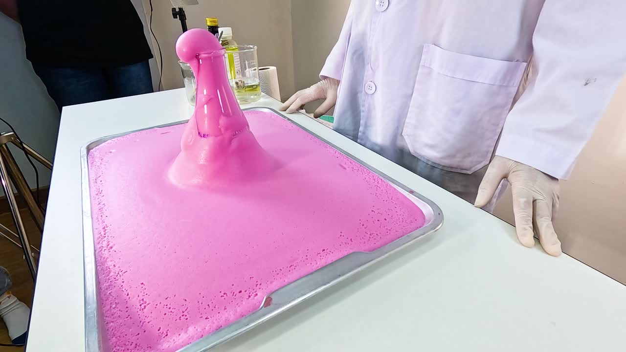 A scientist conducts a colorful elephant toothpaste experiment, creating a foamy pink eruption in a lab setting