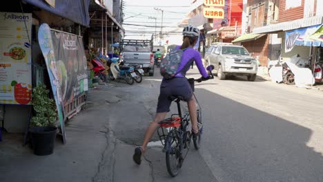 a lady cyclist is riding a cycle on a busy road in thailand