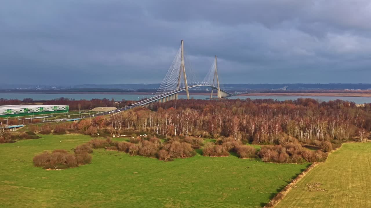 Un drone si avvicina lentamente al Pont de Normandie sopra gli alberi invernali, il traffico e il fiume