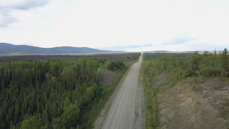 Toma-Aérea-En-Movimiento-Rápido-De-Caminos-En-Mal-Estado-En-El-Campo,-Cordillera-Y-Hierba-En-El-Fondo-En-La-Carretera-De-Alaska