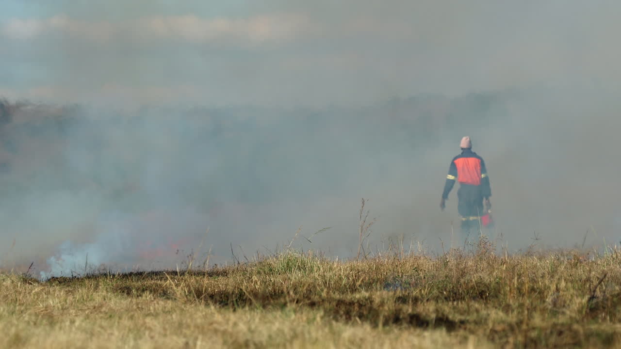 African farm laborer use drip torch on dry vegetation in field for firebreak