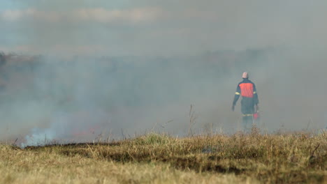 african farm laborer use drip torch on dry vegetation in field for firebreak