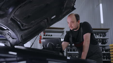 male mechanic uses a tablet computer with an augmented reality diagnostics software. specialist inspecting the car in order to find broken components inside the engine bay. modern car service.