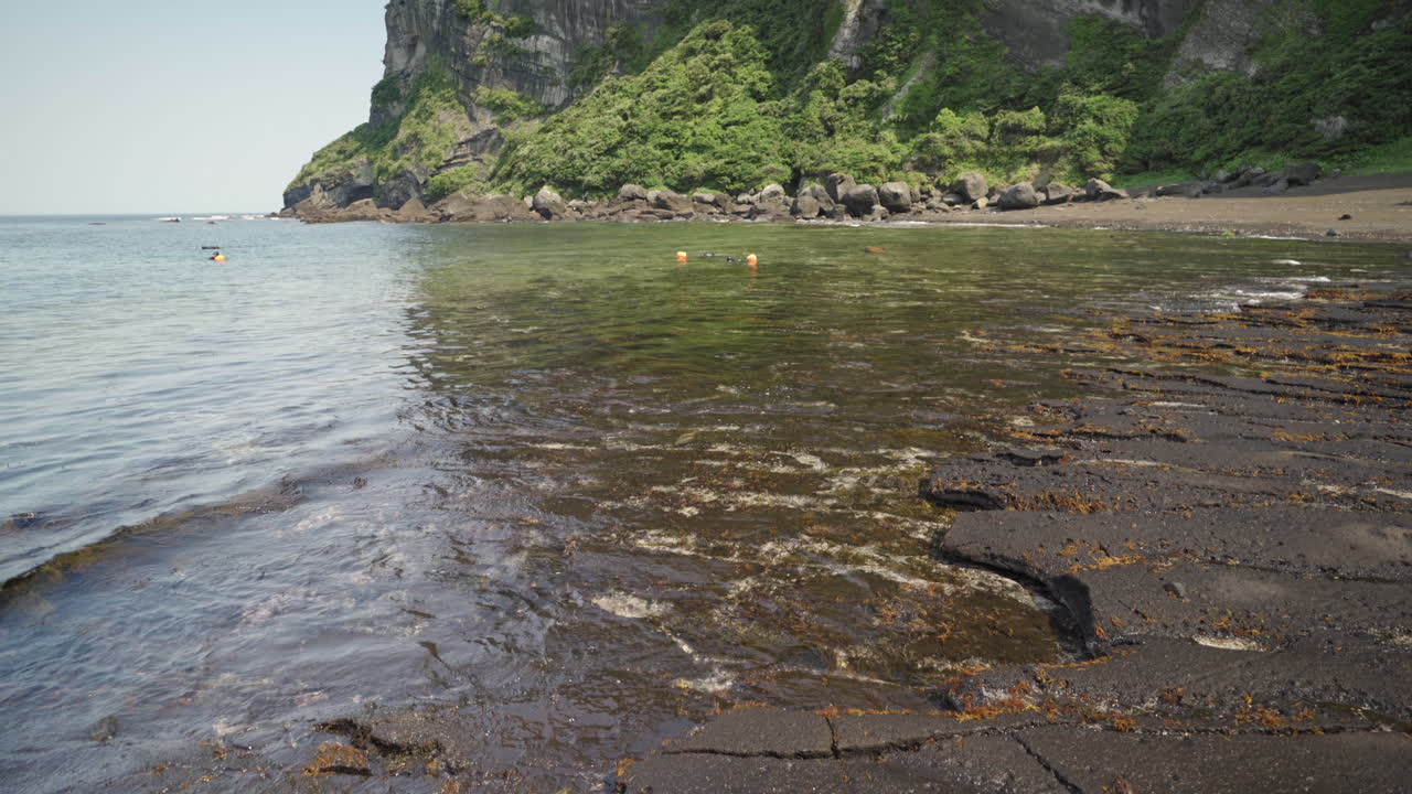 A group of Haenyeo harvesting off the coastline of Seongsan Ilchulbong Peak, Jeju Island, South Korea, medium tilt up in 4K.