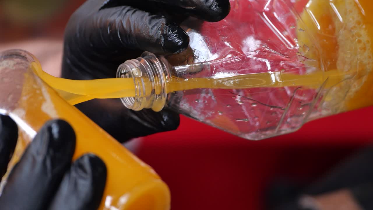 Person in black gloves pouring orange juice from a plastic bottle into a glass bottle