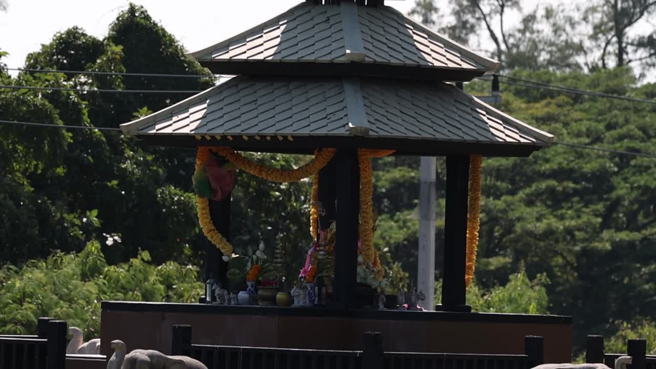 A traditional pavilion adorned with garlands, surrounded by dense green foliage and trees.