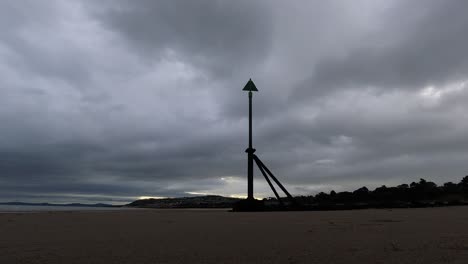 overcast stormy clouds pass above metal high tide marker on sandy beach coastline timelapse