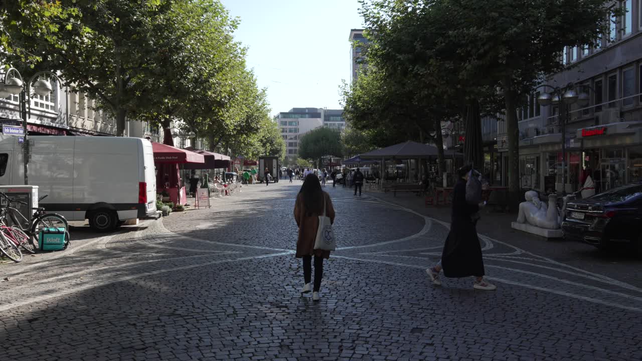 People walking on a cobbled city street lined with shops and trees