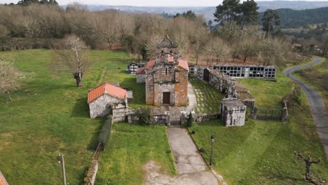 Aerial-pullback-from-moss-covered-bell-tower-and-cemetery-with-dirt-pathway-entrance-to-Church-of-Santa-Maria-de-Vilela-in-Punxin-Ourense-Spain