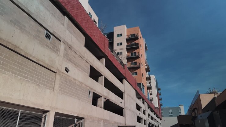 Panorâmica lenta da direita para a esquerda mostrando a parte de trás de uma garagem de estacionamento de concreto com um edifício residencial moderno ou hotel acima