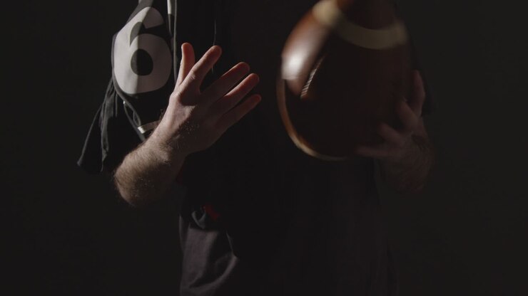 Primer plano de estudio de un jugador de fútbol americano sosteniendo un balón con iluminación de clave baja 2.