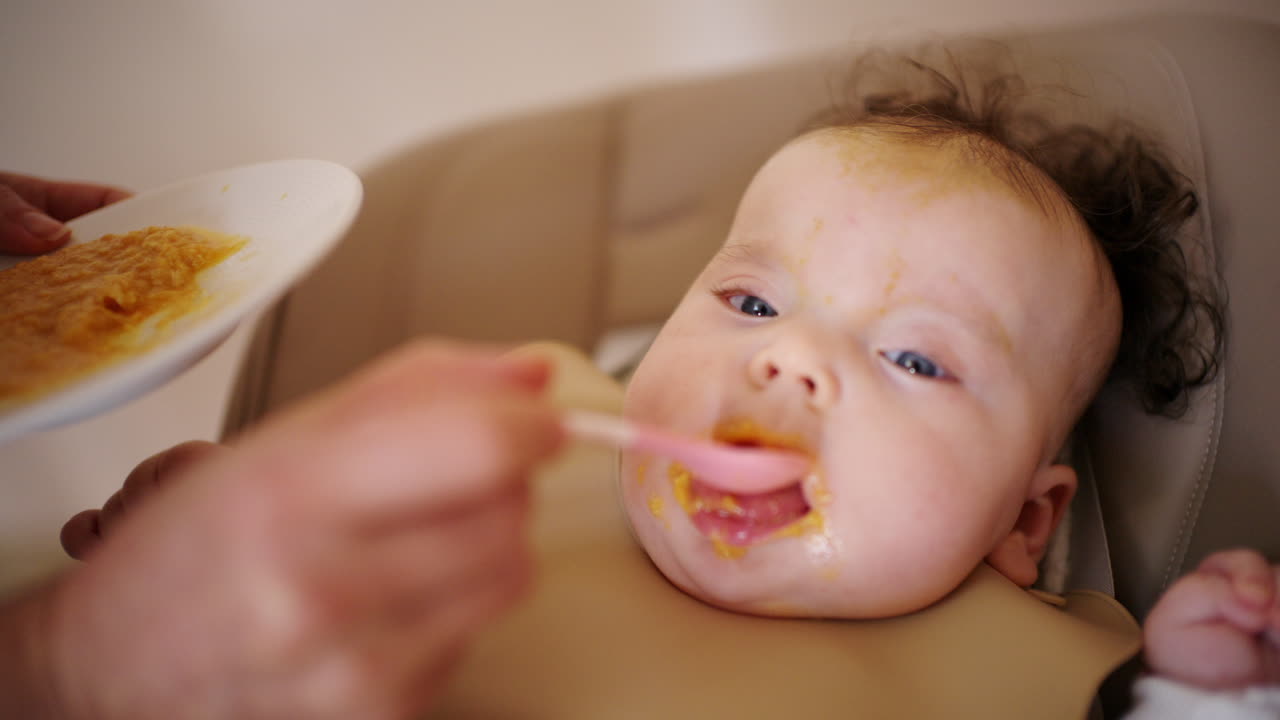 ハイチェアに座る赤ちゃんに大人がスプーンで離乳食を与えている。