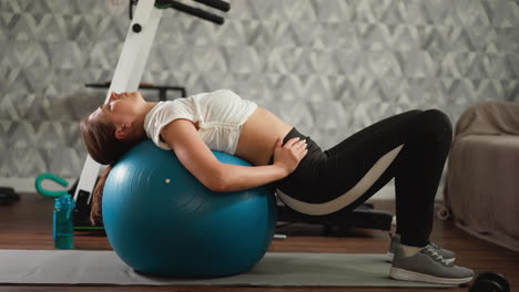 woman works out on fitness ball at home. graceful lady stretches back while training on fitness ball in living room. domestic sport exercise session