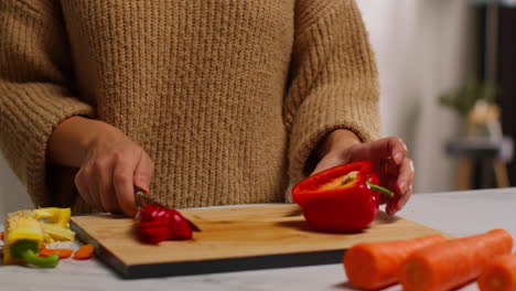 primer plano de una mujer en casa en la cocina preparando verduras frescas saludables para una comida vegetariana o vegana cortando pimienta roja a bordo