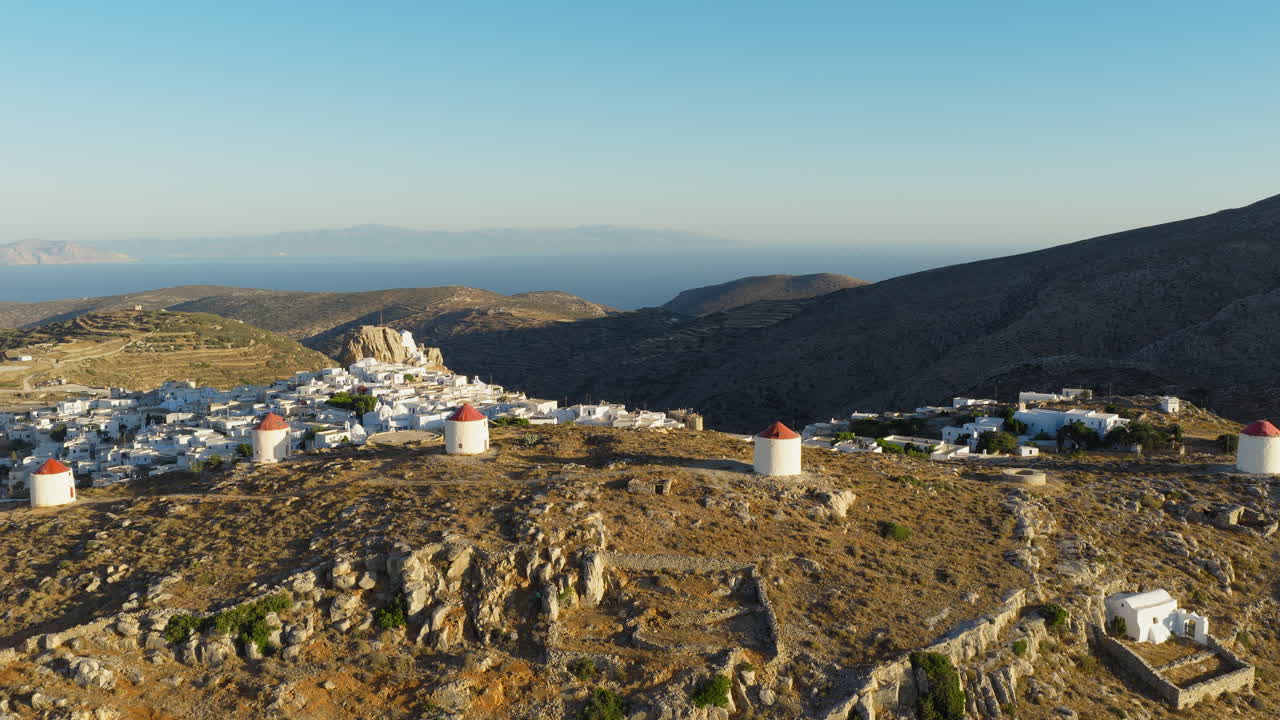 Traditional windmills in Chora on Amorgos island at sunrise surrounded by Aegean sea, Establishing drone shot