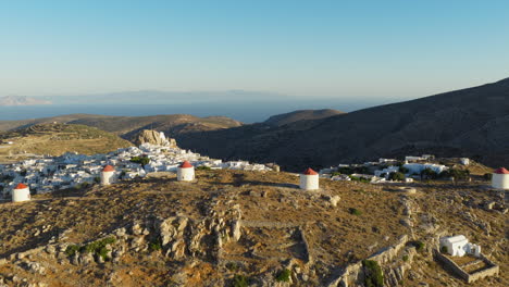 traditional windmills in chora on amorgos island at sunrise surrounded by aegean sea, establishing drone shot