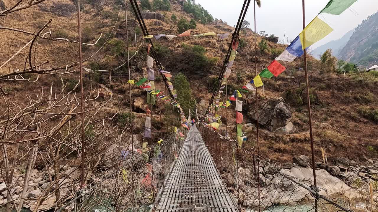 pov atravesando un puente colgante con banderas de oración, suspendido en un valle montañoso, en el impresionante recorrido de langtang en nepal