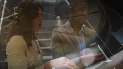 two business people are talking and using a laptop in a corridor of a modern office