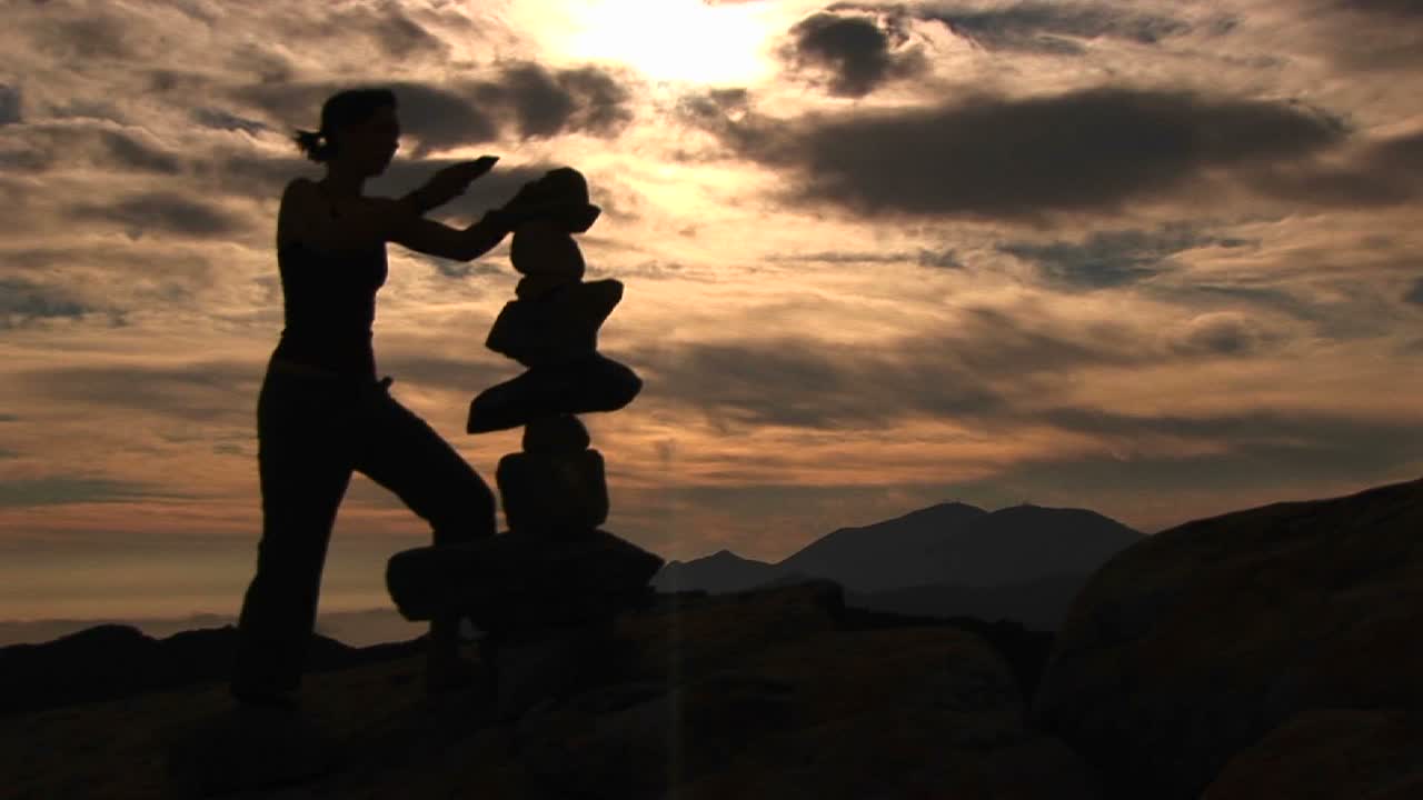 산꼭대기에 바위를 쌓고 있는 실루엣 여자의 미디엄샷