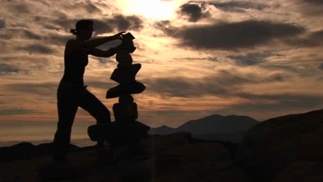 mediumshot of a silhouetted woman stacking rocks on a mountaintop