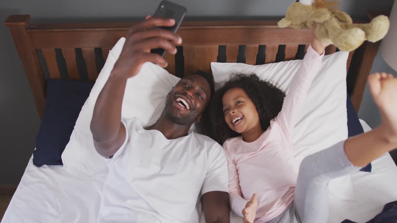Padre e figlia afroamericani che si fanno un selfie a letto
