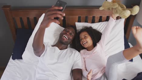 african american father and daughter taking selfie in bed