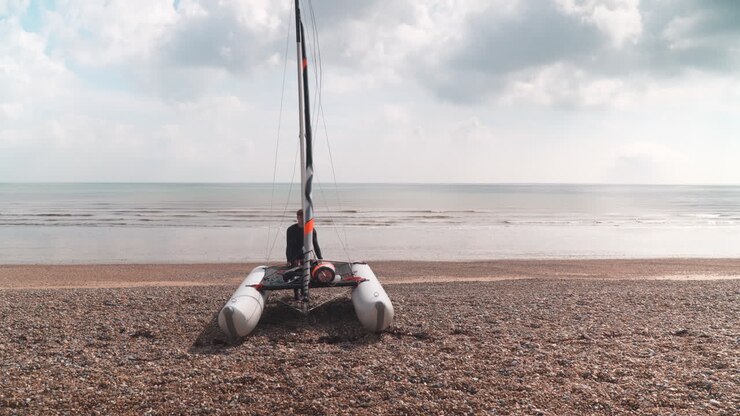Man dragging his catamaran down pebble beach towards the sea