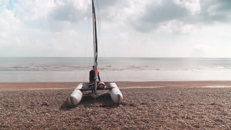 Man-dragging-his-catamaran-down-pebble-beach-towards-the-sea