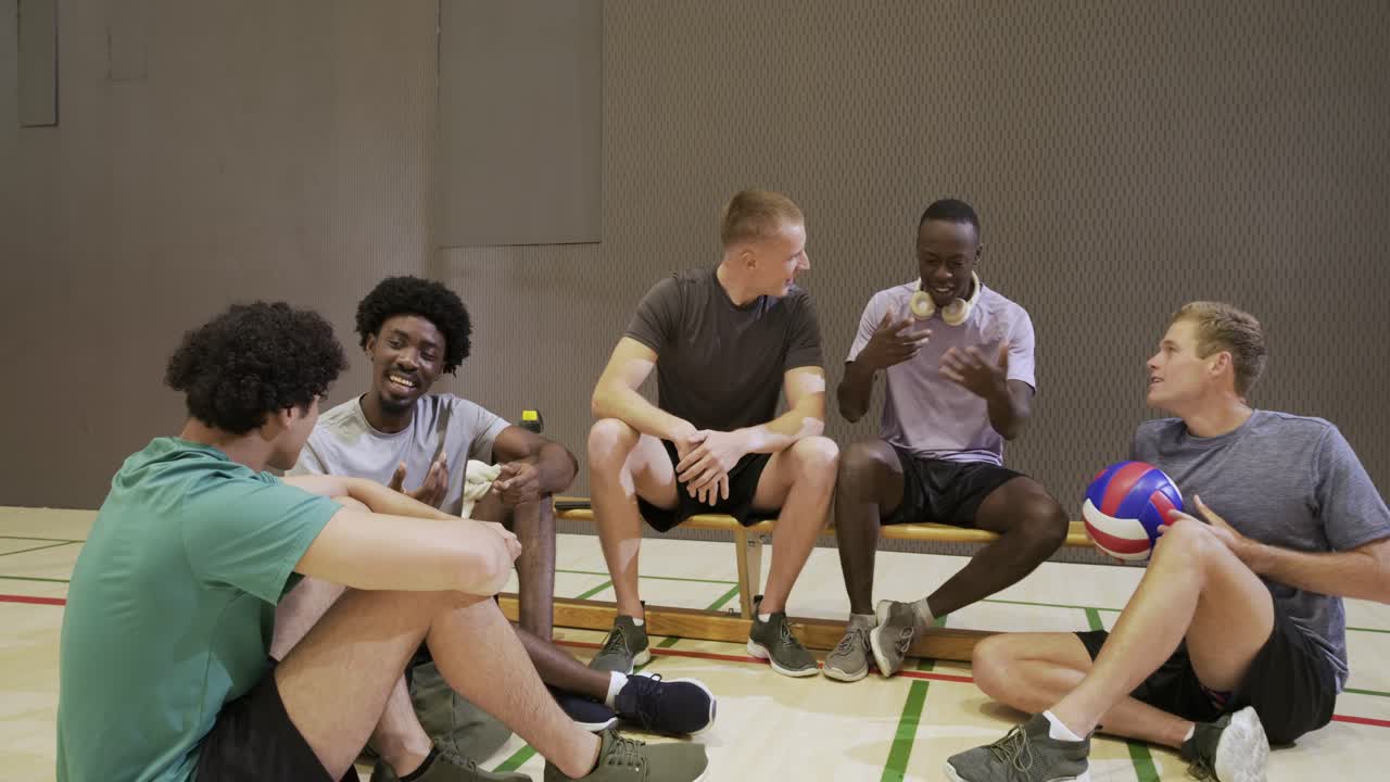 Efter træning hviler forskellige mandlige atleter på en bænk på gymnastikbanen, kaster volleyball og griner.