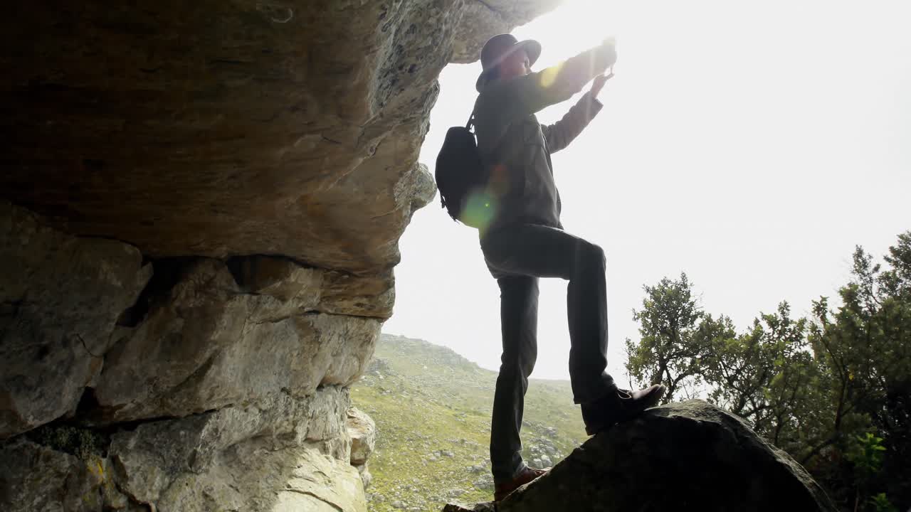 excursionista masculino tomando una foto con un teléfono móvil cerca de una cueva 4k