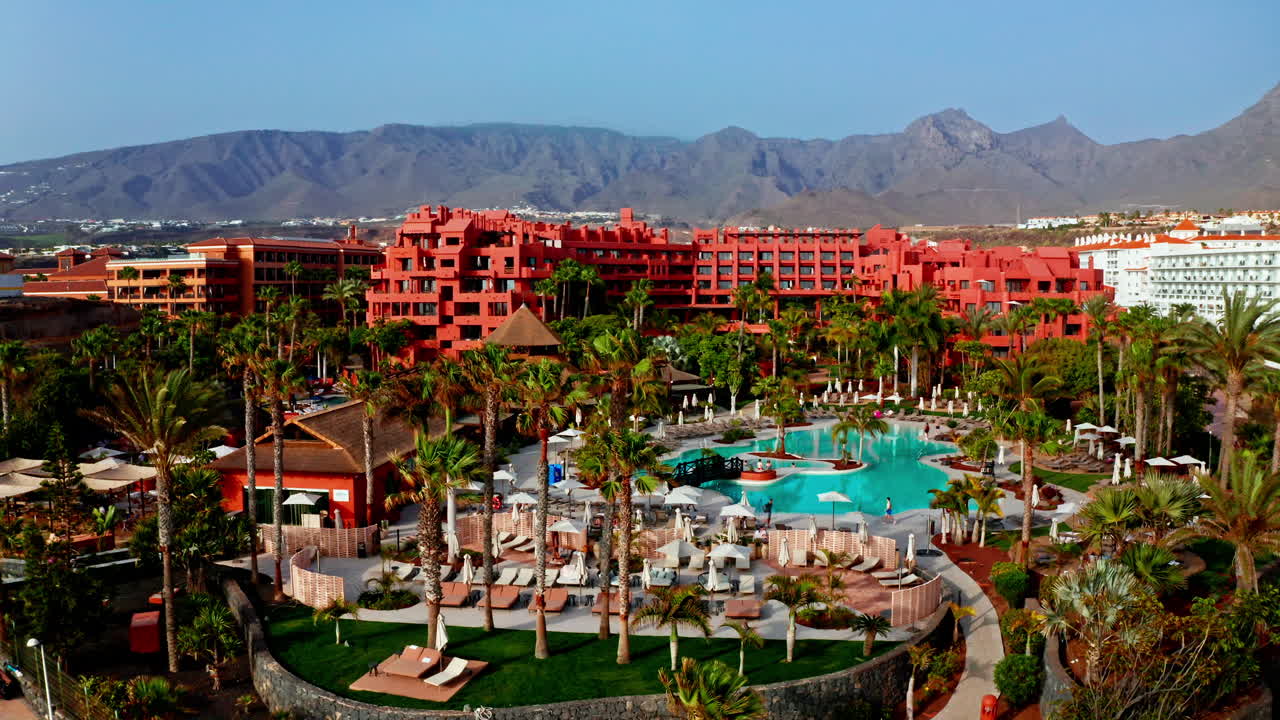 Ripresa aerea con drone su un bellissimo resort sulla spiaggia a Tenerife, Isole Canarie, Spagna. Vista dall'alto della struttura, delle piscine all'aperto e delle alte palme. Destinazione per le vacanze estive per i turisti.