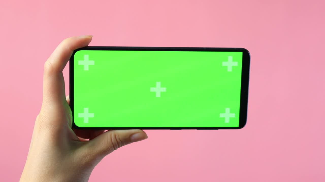 primer plano de manos femeninas sosteniendo un teléfono inteligente con una pantalla verde en blanco que muestra espacio de copia para el diseño de aplicaciones o sitios web, en fondo rosa, maqueta.