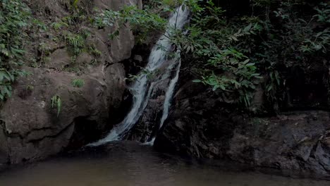 Panorámica-Lenta-Retrocediendo-Desde-La-Desembocadura-De-Una-Cascada-Para-Revelar-Un-Pequeño-Estanque-Y-Un-Entorno-Rocoso-Más-Amplio-En-El-Bosque-Tropical-De-Montaña-En-Río-De-Janeiro