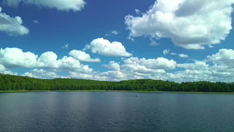 white clouds in a blue sky over a vast lake with forests on the shore