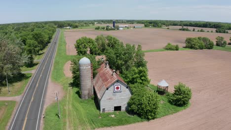 low panning aerial shot of an old barn with a silo in the farmland of minnesota