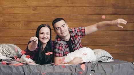 romantic couple are lying on the bed and throwing red paper hearts with their hands on valentine's day