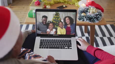 African-american-mother-and-daughter-using-laptop-for-christmas-video-call-with-family-on-screen