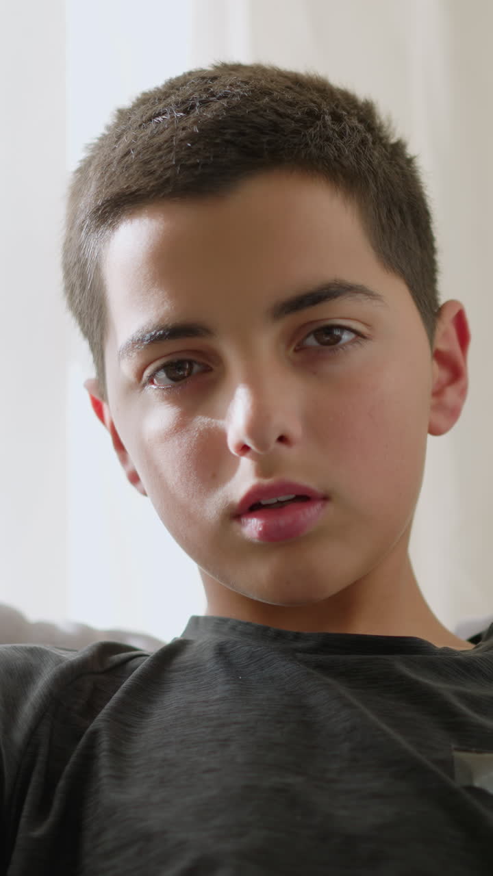 Portrait view of sick boy resting on the couch, looking weak and exhausted, wrapped in a blanket, with tissues scattered around, showing his tired, unwell state