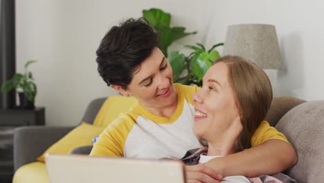 Caucasian-lesbian-couple-smiling-while-having-a-videocall-on-laptop-on-the-couch-at-home