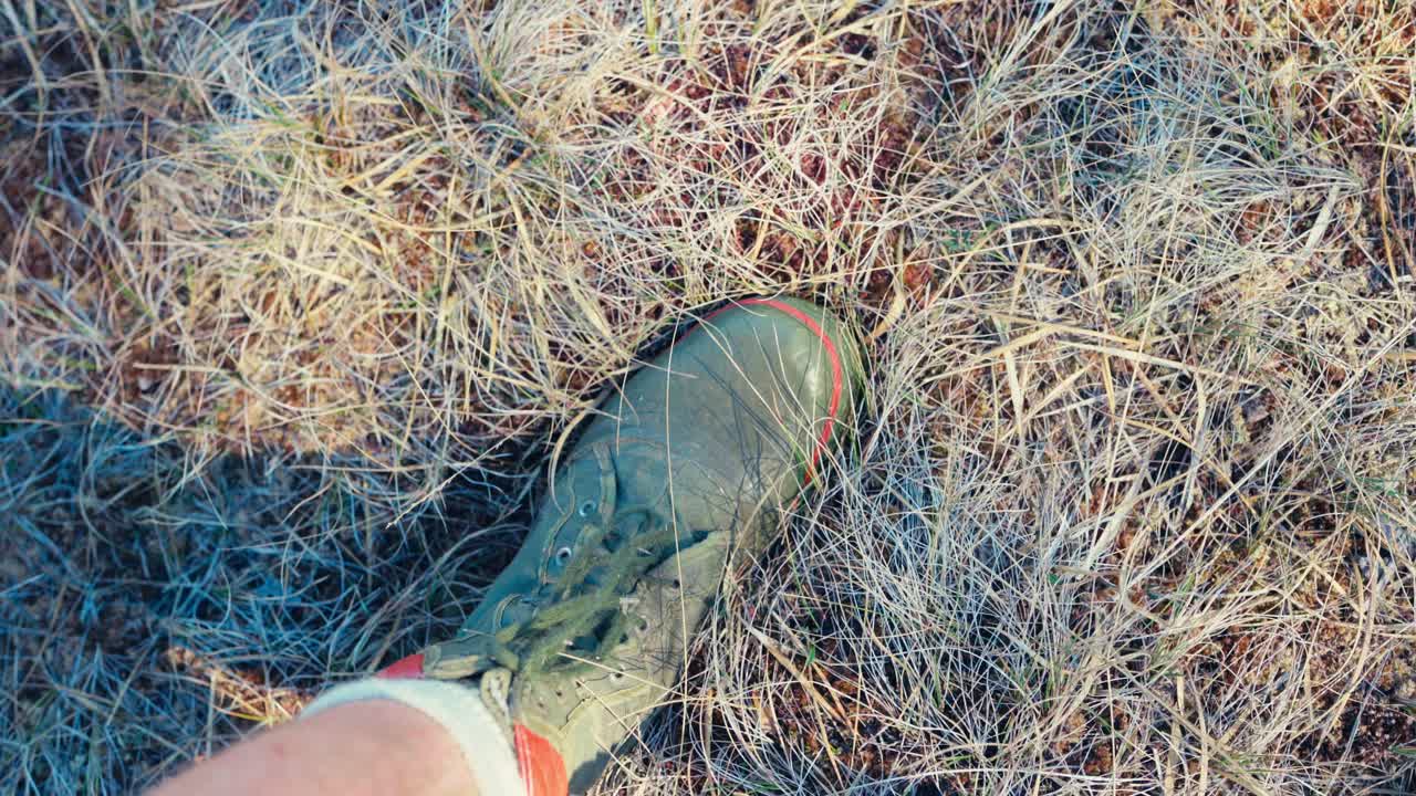 Piede di un uomo con scarpa da trekking che calpesta erba secca su un campo