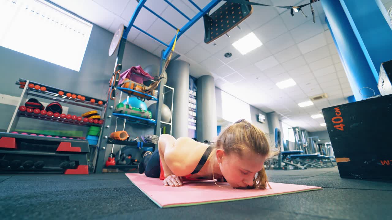 Beautiful girl doing exercises on a mat. Young woman in sportswear doing push-ups workout in the modern fitness centre.