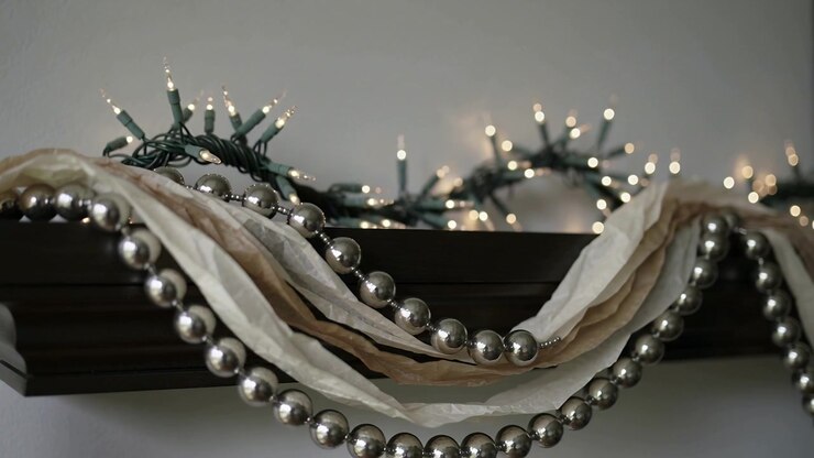 Shifting camera revealing metallic silver bead garland and ribbons on mantel, showing warm lights